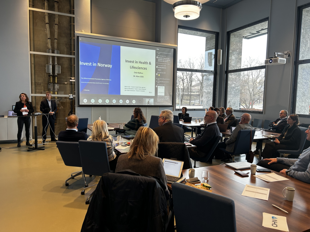 To personer står ved en skjerm, og mange mennesker ser mot skjermen