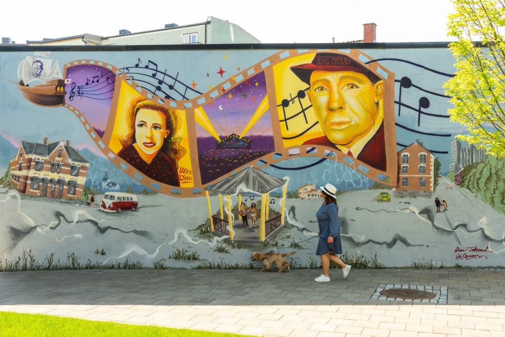 Street Art i Mysen av kunstner Olav Tokerud, bilde av dame og hund som går foran motiv. Foto av Jonas Ingstad / Visit Indre Østfold.